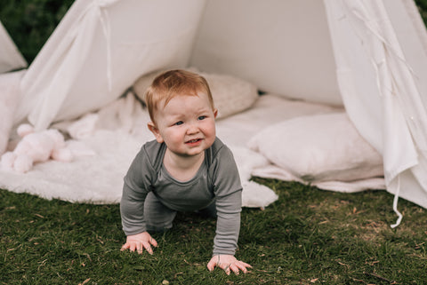 Baby crawling toward the camera onto the grass from a rug.