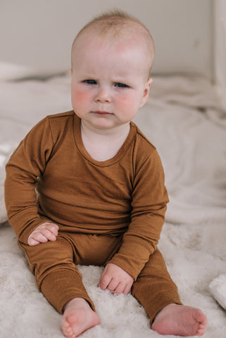 Baby sitting up looking at the camera wearing a merino sleepsuit.