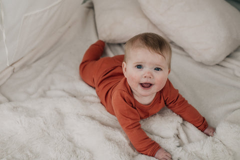 Baby lies on soft blanket smiling up at camera in Red Clay pyjamas