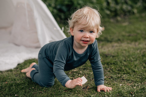 Baby crawls on grass towards the camera wearing merino soft teal pyjamas