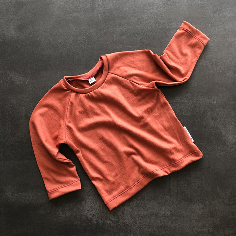 Flat lay of the merino raglan tee in Red Clay.