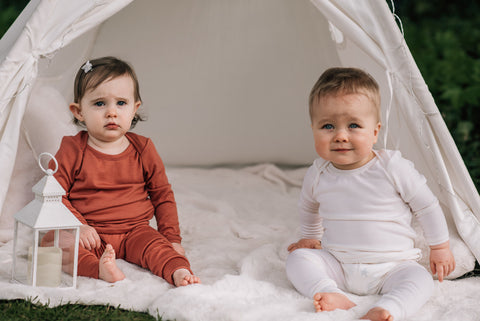 Two babies wearing Merino wool pyjamas sitting in a play teepee