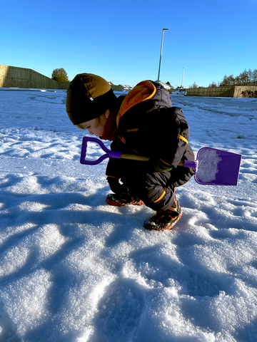 Merino Dot Baby CTO bending down to look closely at the snow with his spade in hand.