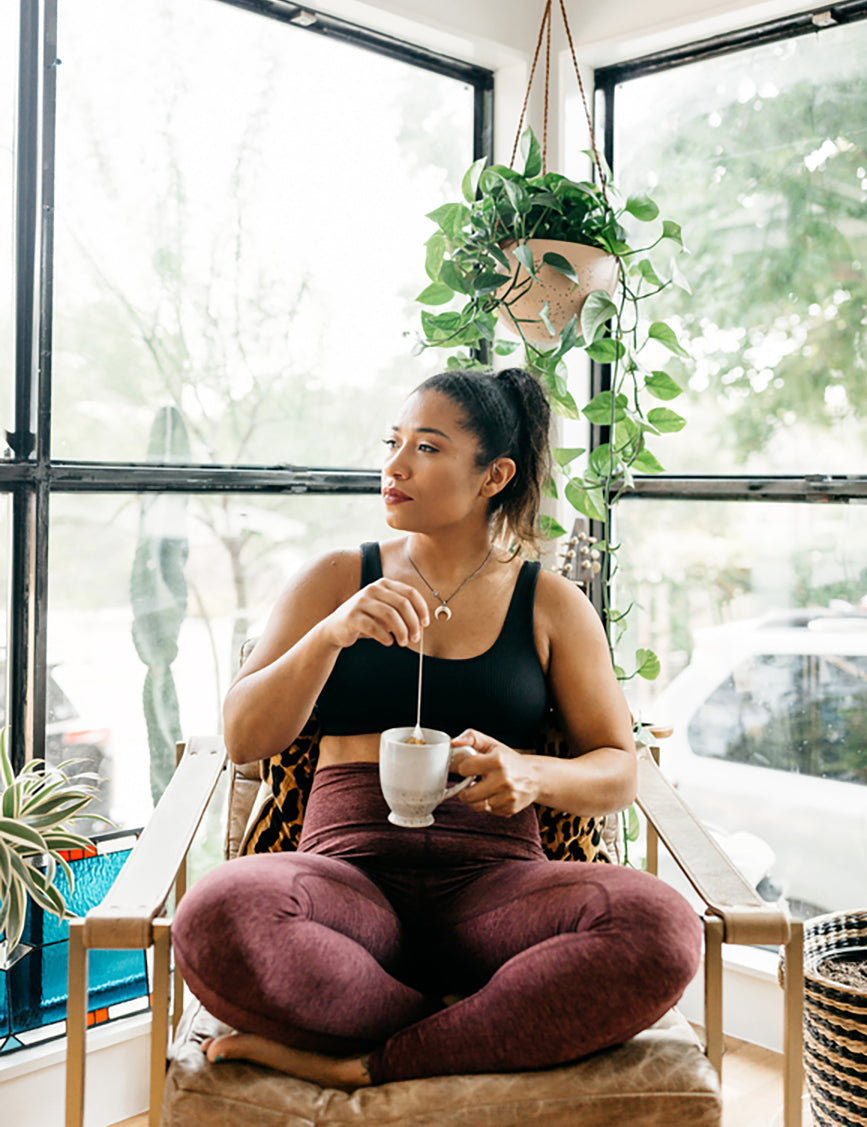 woman drinking tea on a chair next to a plant