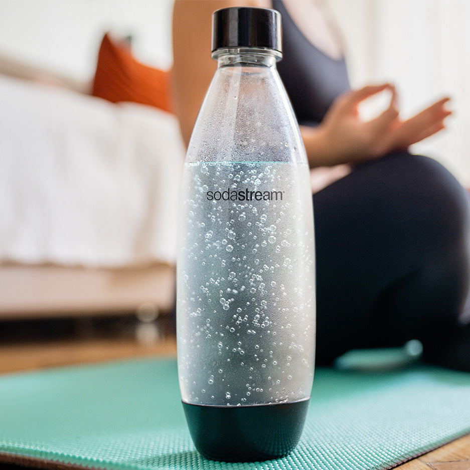 Butelka SodaStream z wodą gazowaną i kobieta podczas jogi