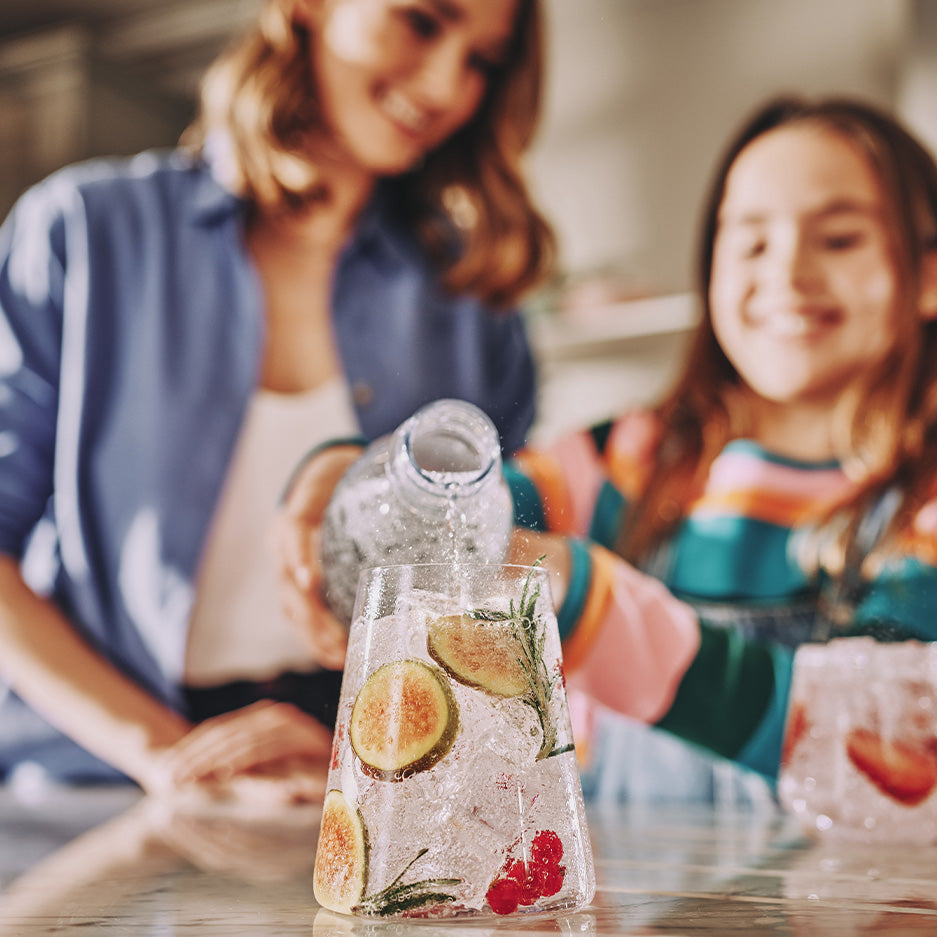 Matka z córką nalewający wodę gazowaną SodaStream do szklanki z dodatkami