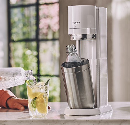 Saturator SodaStream i ręka nalewająca wodę gazowaną do szklanki - tytułowa.