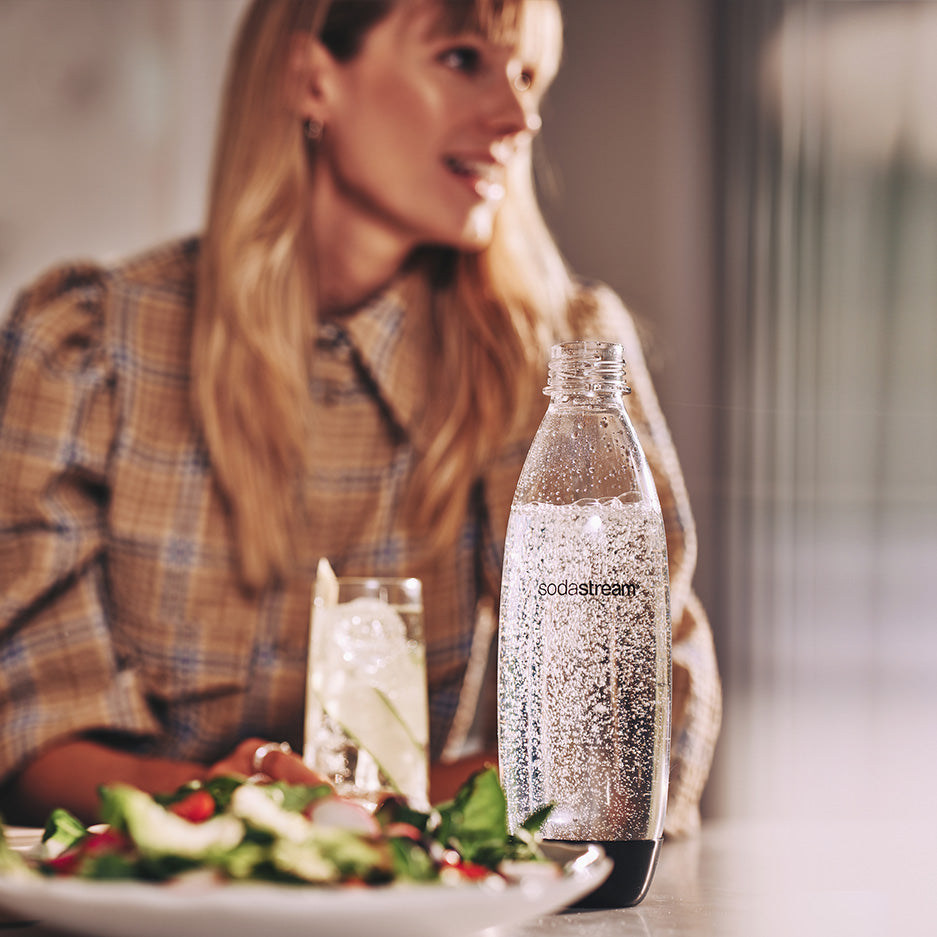 Rozmawiająca przy stole kobieta z butelką SodaStream - tytułowa.