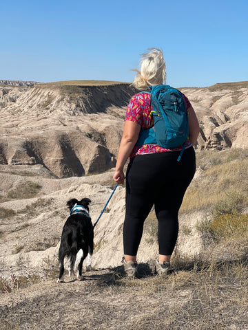 Jenny, the founder of Unlikely Hikers, and Big Judy the Border Collie mix take in the view while hiking on a warm, sunny day.