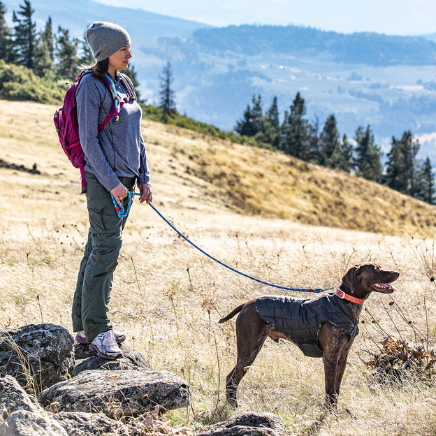 A woman stands on a rock with her dog wearing the black Loft Jacket.