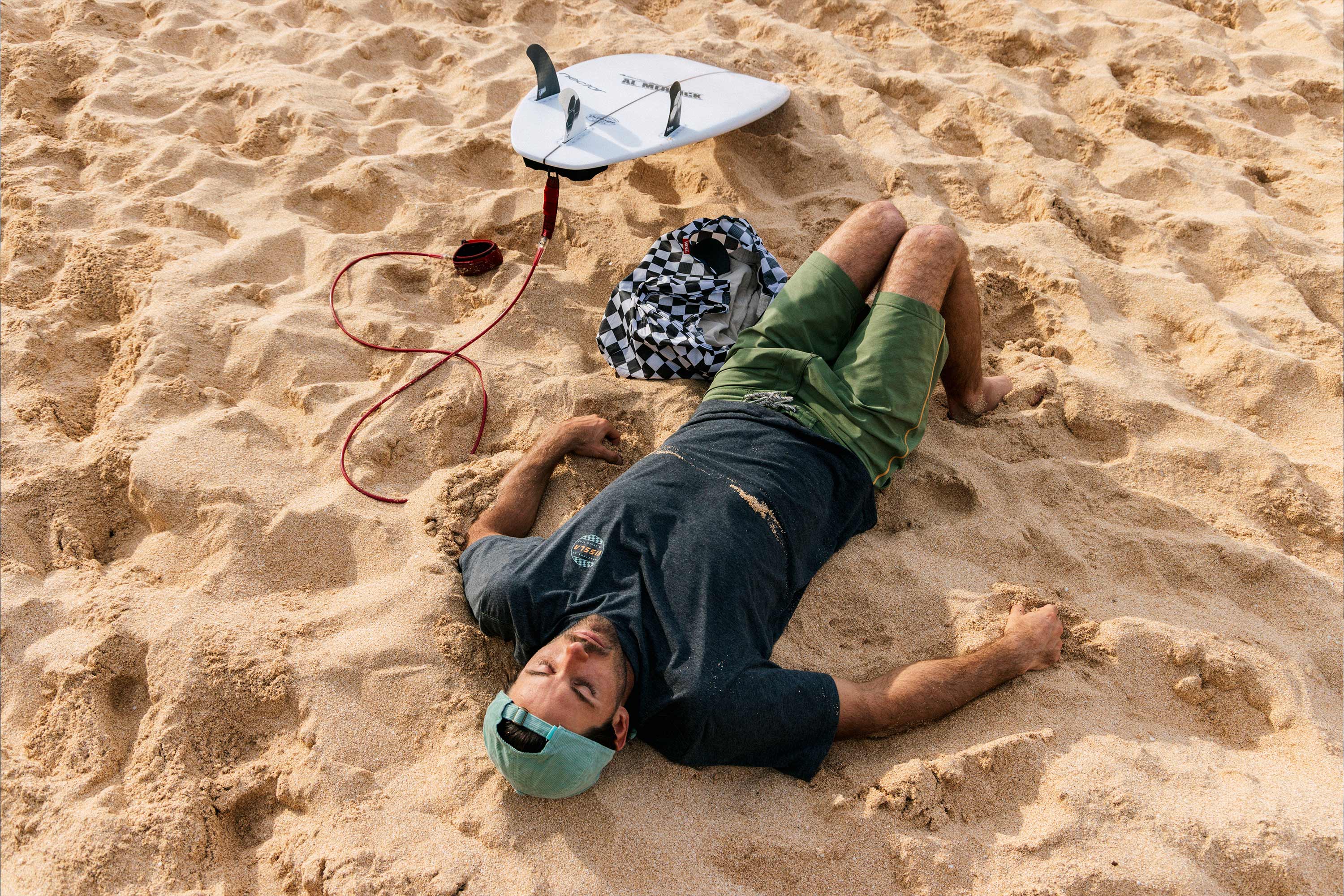 cam richards laying on the beach in hawaii after surfing in his vissla solid sets boardshorts