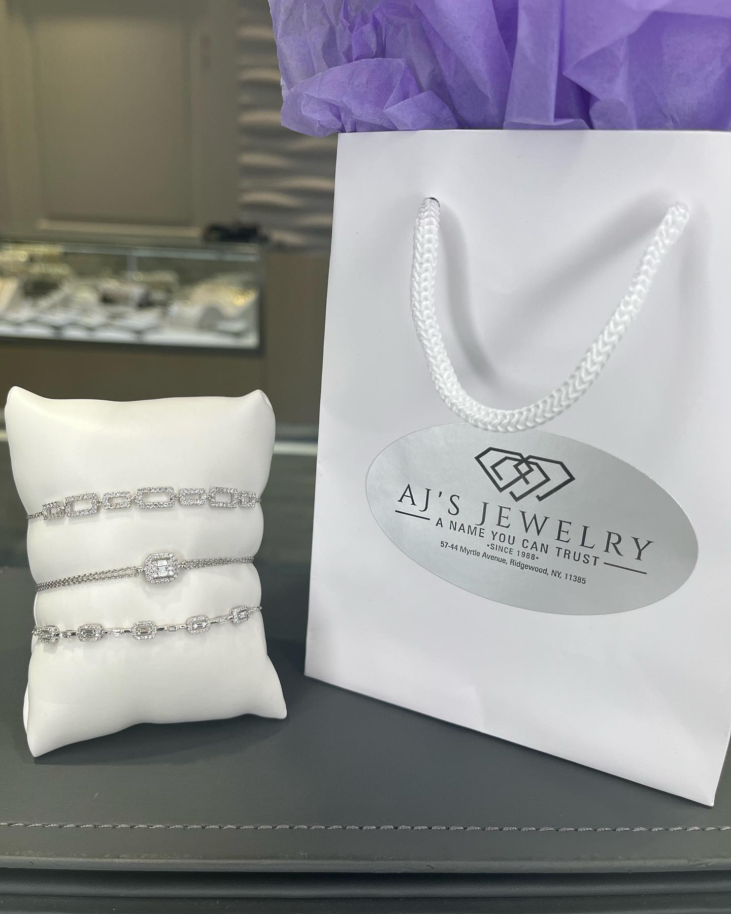 Silver diamond necklace on a white fabric pillow next to the white paper bag
