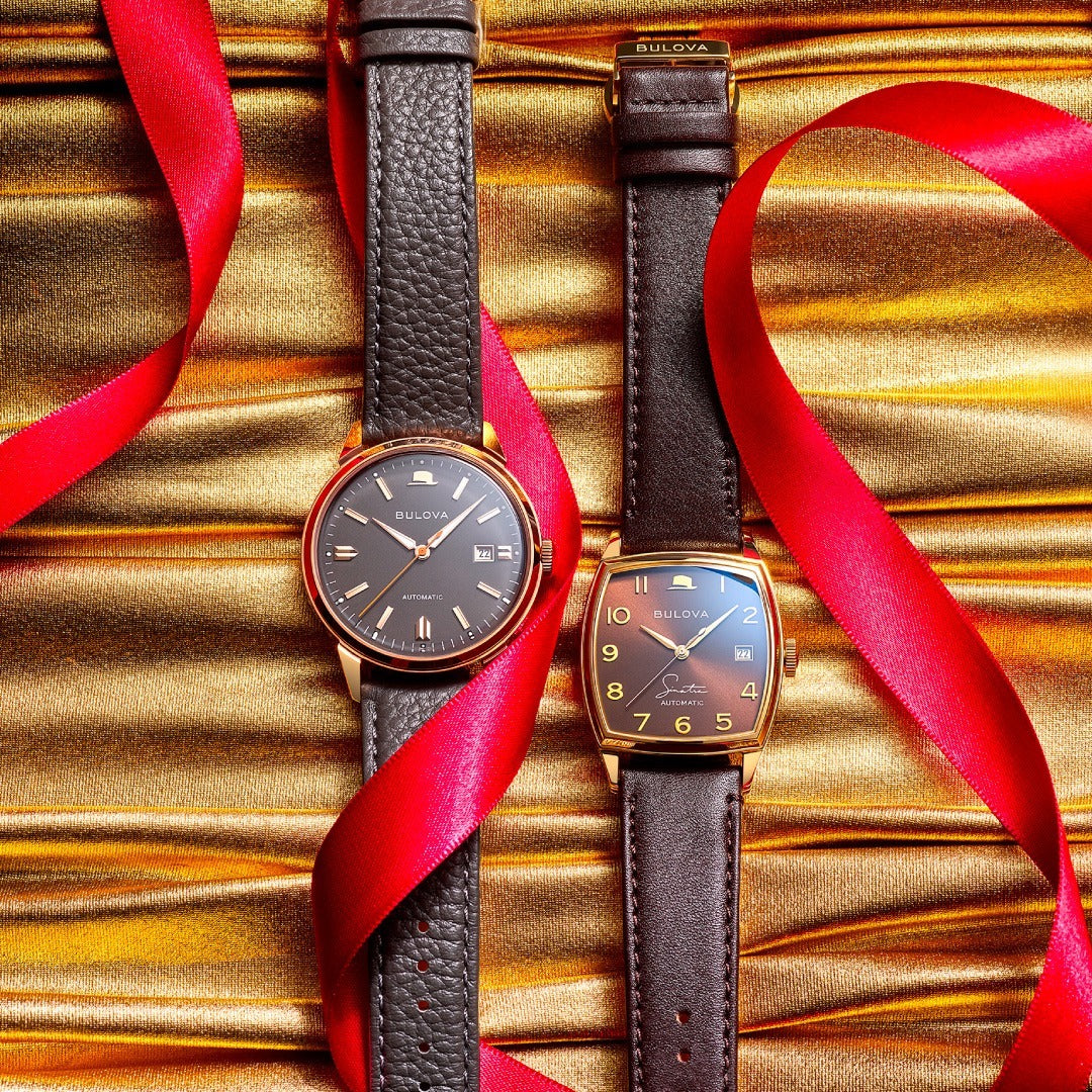 Two watches has a  dark brown leather strap resting on a gold fabric with red laces