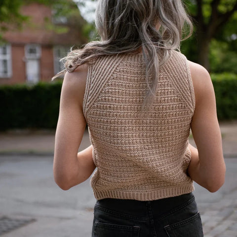 a woman facing away from the camera wearing a beige handknitted top