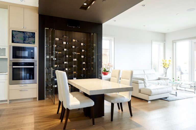 Dining room with open doored dark-hued colored wine display, overlooking white modern living room.