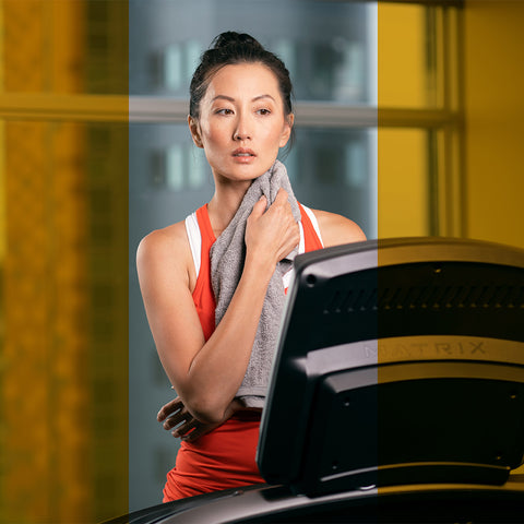 woman wiping neck with towel on exercise equipment