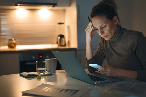 woman with a laptop and a cell phone looking stressed