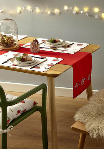 A table draped in a red table runner with robin decoration, and complemented by a red placemat.