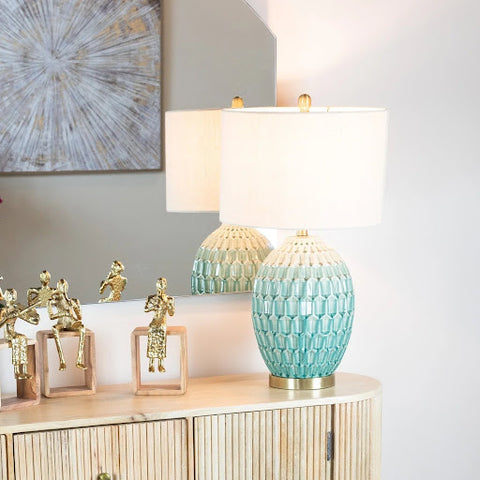 A lamp with an aqua colour base and cream-coloured shade sits on a side table in a hall.