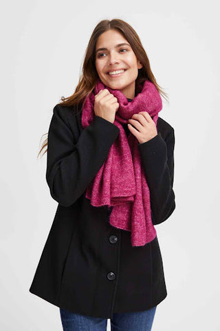 the model wears a bright pink chunky knitted scarf with a black overcoat and jeans.