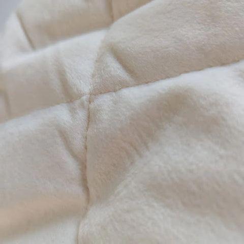 Close-up of a soft, fleece mattress enhancer from Shaws, showing its plush, textured fabric in a creamy white shade. The detailed stitching creates a quilted pattern, suggesting a comfortable and luxurious addition to a bed's comfort.