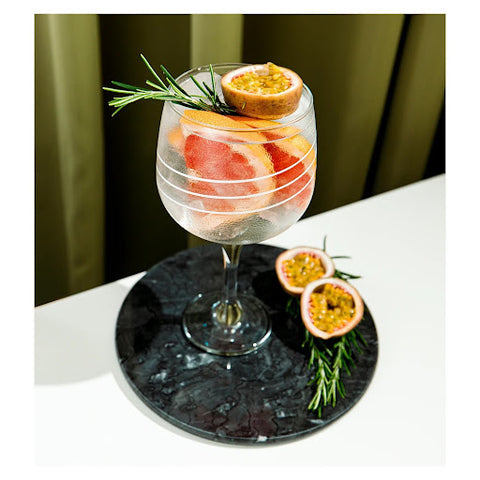 A gin glass made of crystal, with three white lines circling it as the design. The glass is filled with gin and pink grapefruit.