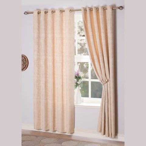 A pair of champagne-coloured eyelet curtains drape from a decorative rod.
