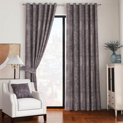 Thick, graphite-colored curtains with a ring-top design are drawn open in a furnished room. The room features a chic white armchair, a white lamp on an end table, and a white cabinet with blue decorative vases.