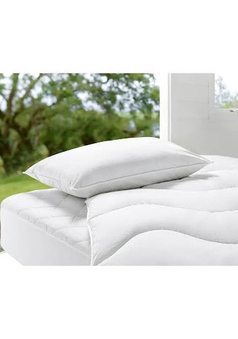 A white duvet and white pillow on top of a mattress in front of a window looking out to a garden.