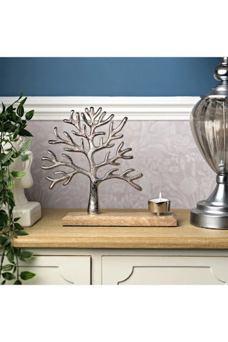 A close-up of a silver tree ornament and candle on a side table in a hallway. The wall behind is blue, with floral patterned wallpaper underneath.