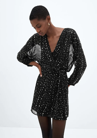 A woman is wearing a black and white printed wrap dress with long sleeves. The dress is cinched at the waist.