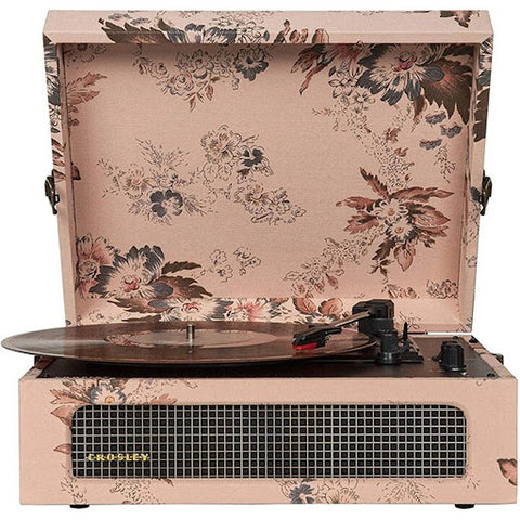 A briefcase design pastel pink record player with delicate floral designs, a grill at the front where the two speakers are located behind.