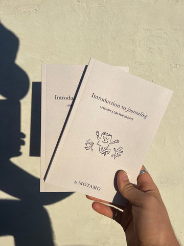 Picture of 2 notebooks held by hand in front of a  concrete beige background.