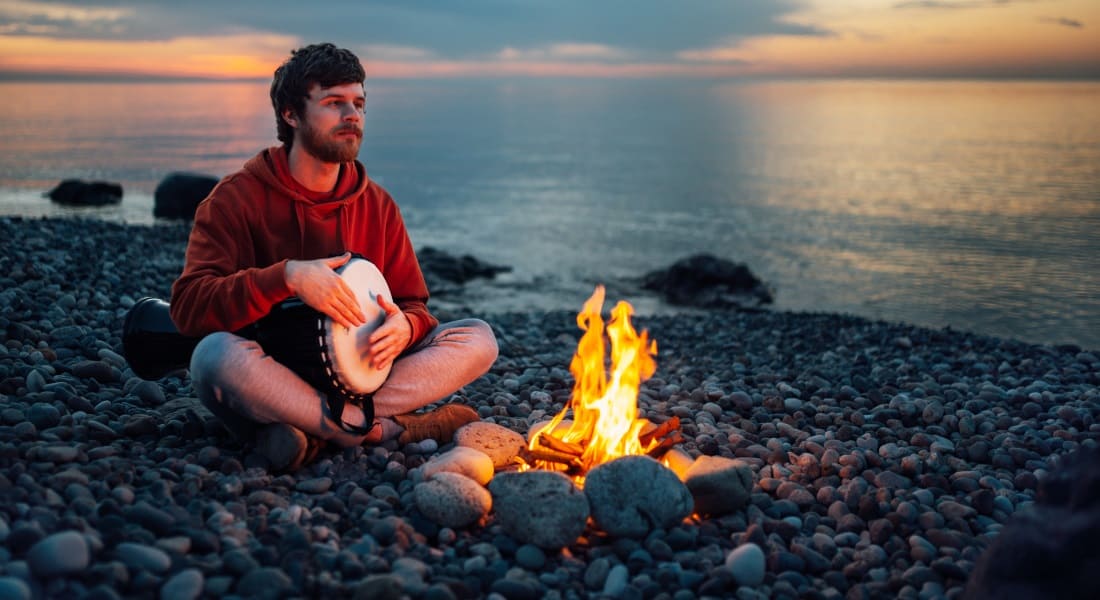 Un homme assis près d'un feu avec un Djembé