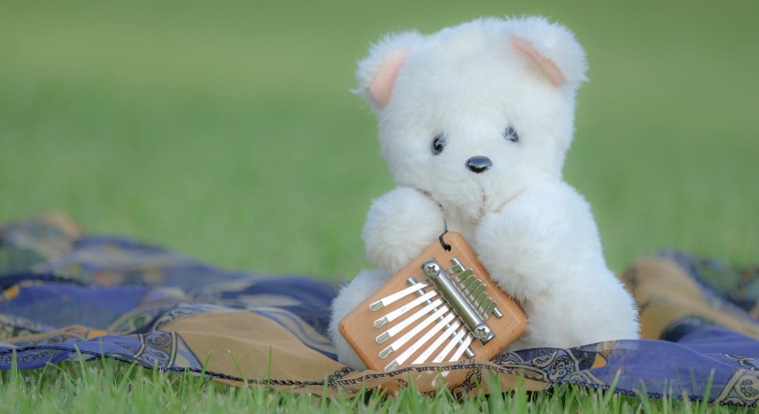 Un ours en peluche dans l'herbe qui tient un Kalimba entre ses pattes