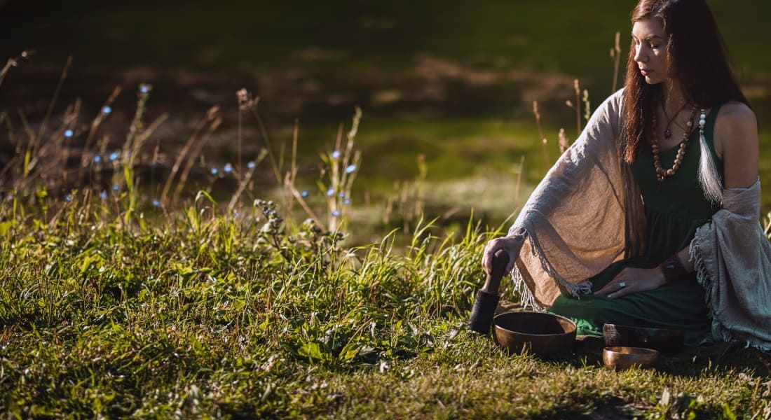 Une femme assise dans l'herbe qui Médite avec un Bol Chantant