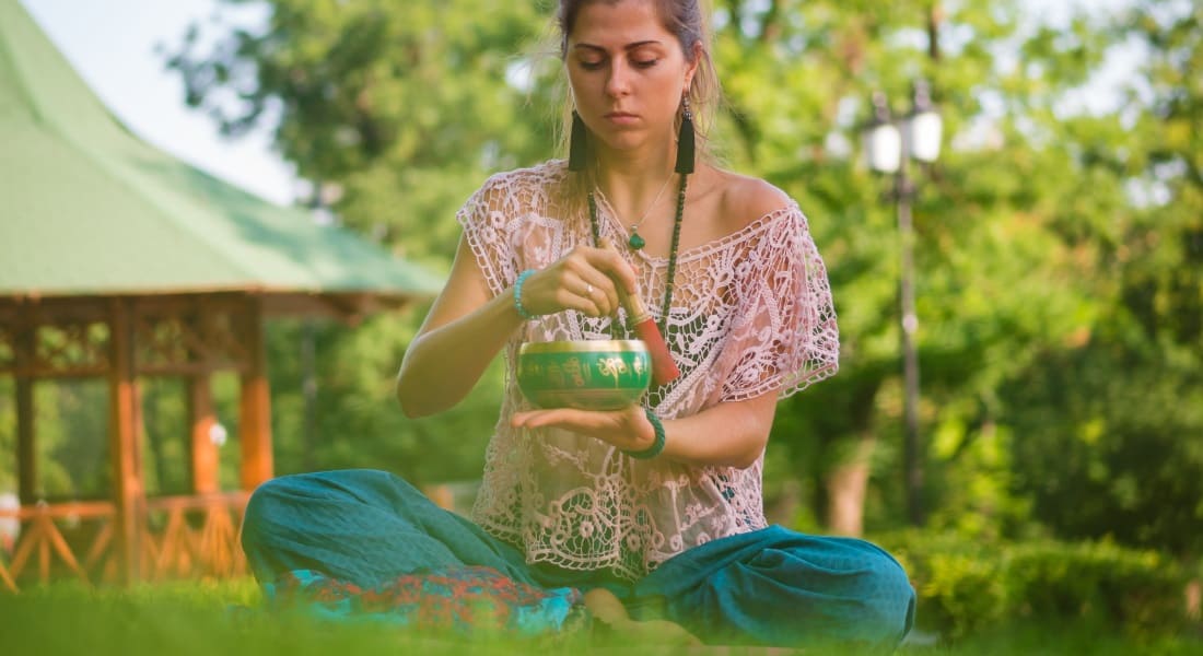 Une femme assise dans l'herbe qui médite avec un Bol Chantant