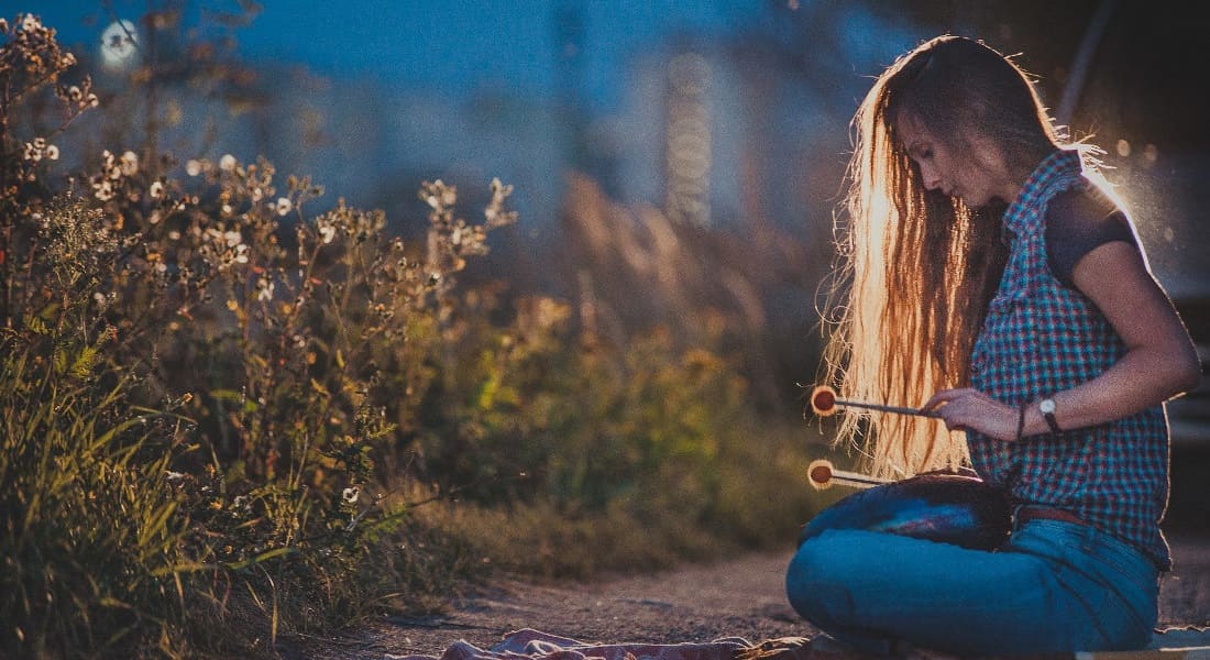 Une femme assise en tailleur sur le sol avec un Tongue Drum dans la nuit