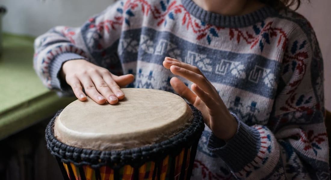 Une femme avec un pull qui utilise un petit Djembé