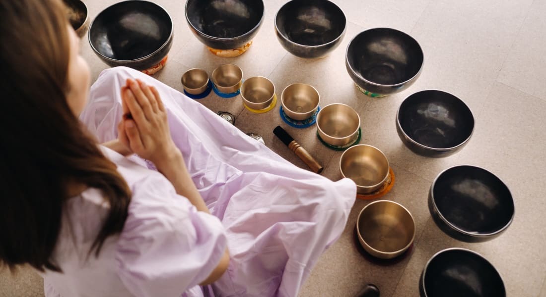 Une femme de dos qui Médite entourée de Bols Chantants