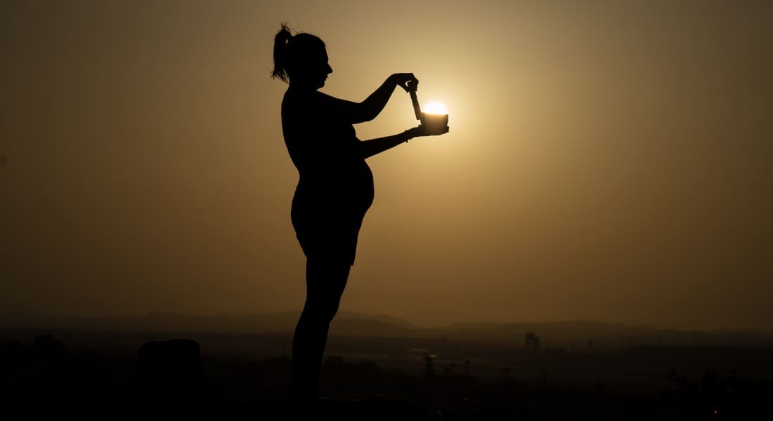 Une femme enceinte avec un Bol Tibétain devant un coucher de soleil