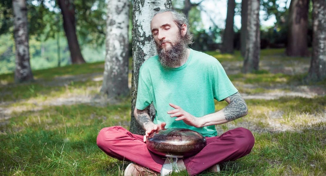 Un homme assis dans la forêt jouant du Tongue Drum