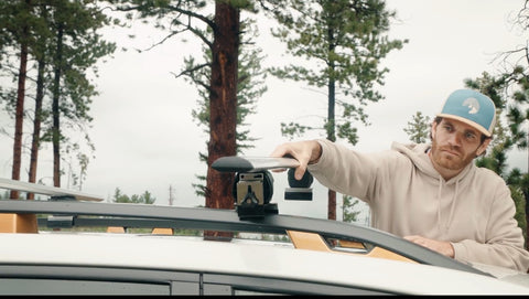 A man touching a car roof rack in the woods.