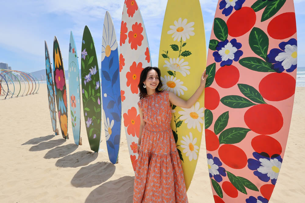 Photo of the model at the beach with some surf boards behind her