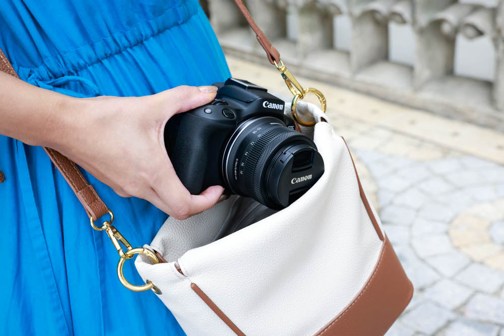 Lifestyle Image of the Canon RF-S 10-18mm attached to a camera and slipped into a ladies purse to help illustrate the compact size of the camera