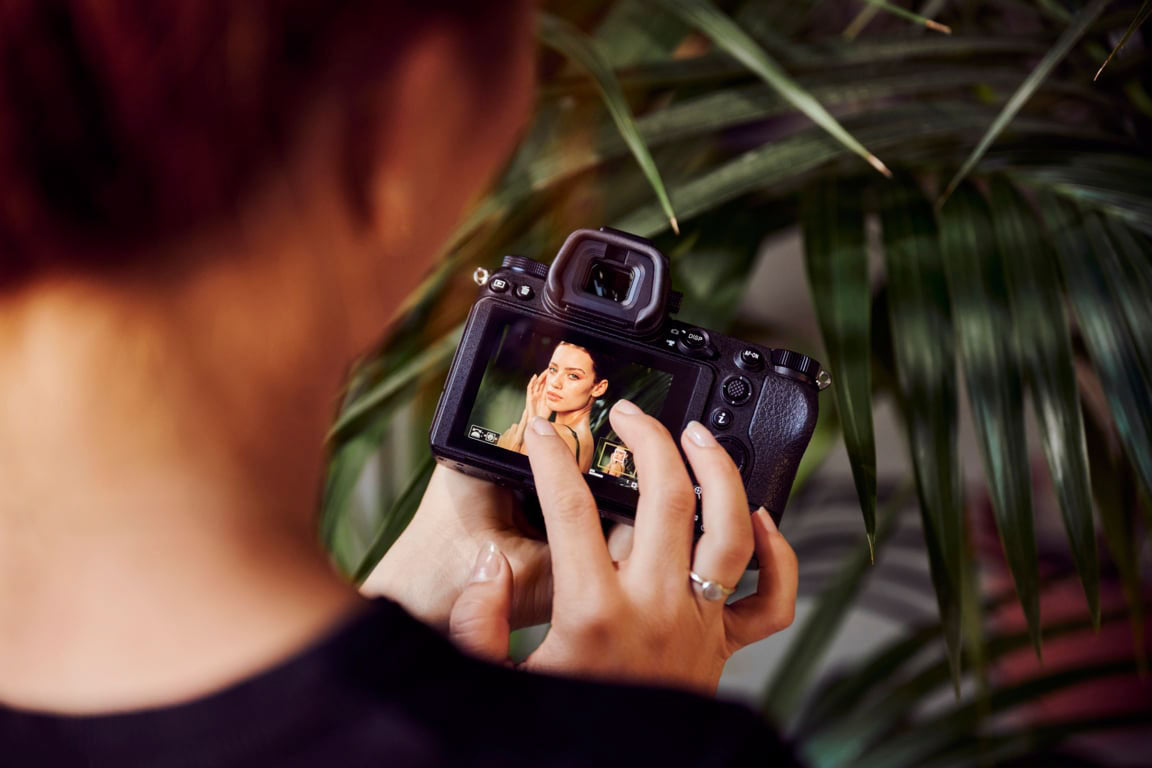Improved Ergonomics on the NIkon Z7ii - Showing a lady holding the camera with a nice plant in the background. That's nice