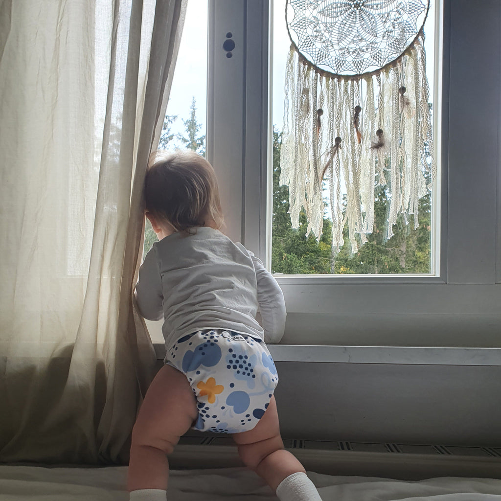 Bebé de Judes delante de ventana con atrapasueños, pañal siempre deslizándose