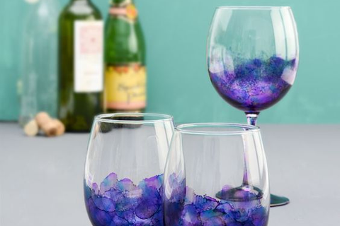 A wine glass and two other glasses decorated with purple and blue alcohol ink.