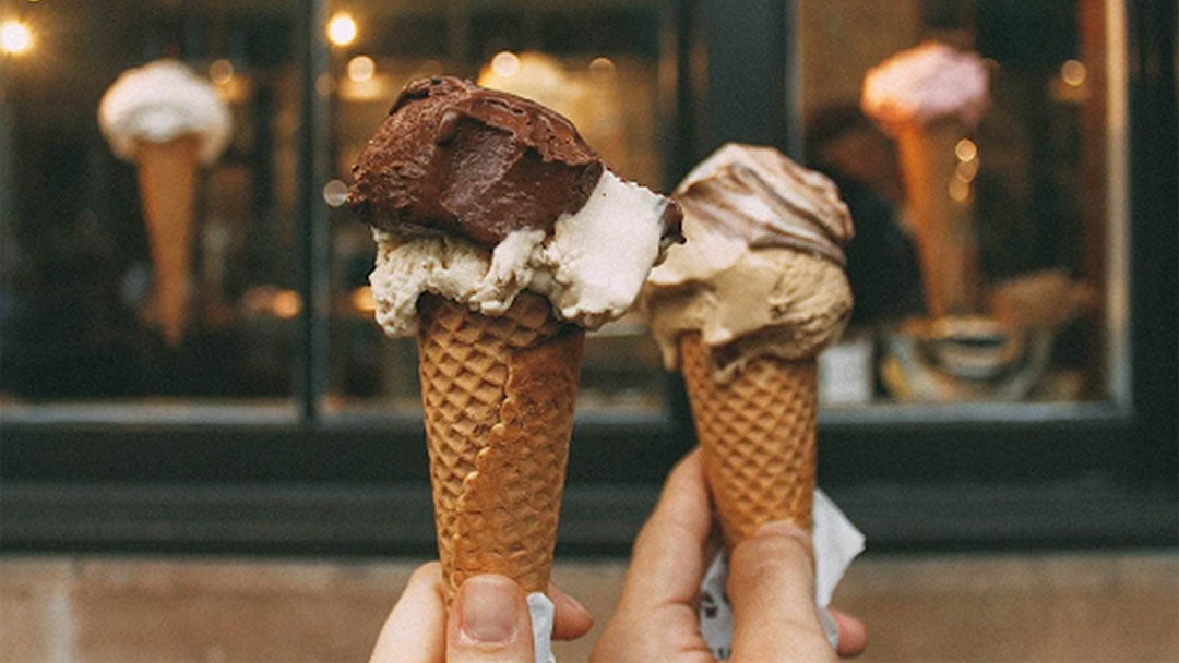 Two hands holding chocolate and vanilla ice cream cones.