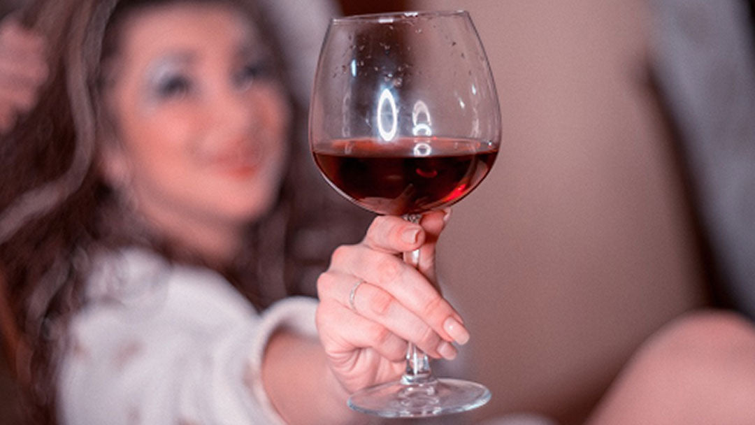 Woman holding a wine glass stem filled with red wine.
